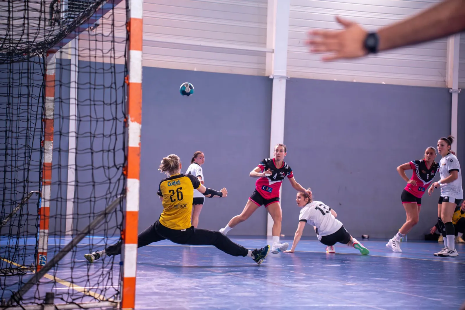Dynamic action shot of a women's handball match with players in mid-movement.